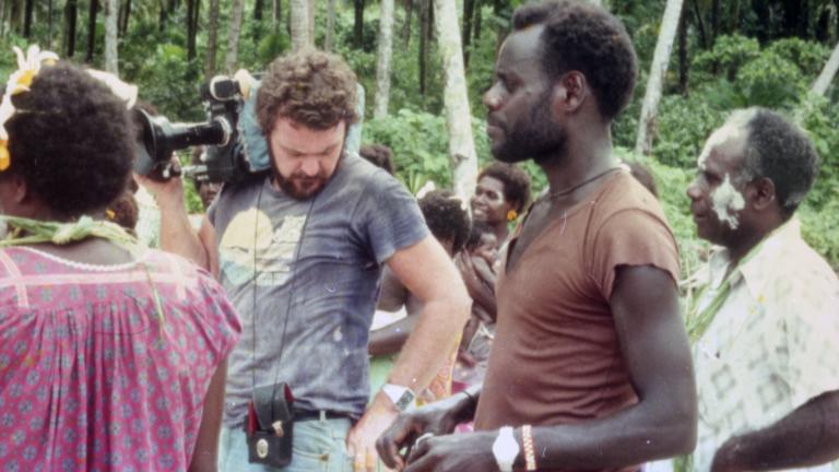 Co-director Chris Owen holds a film camera on his shoulder and stands next to co-director and star Albert Toro and other actors on location for the 1982 film Tukana in the Papua New Guinea Highlands.