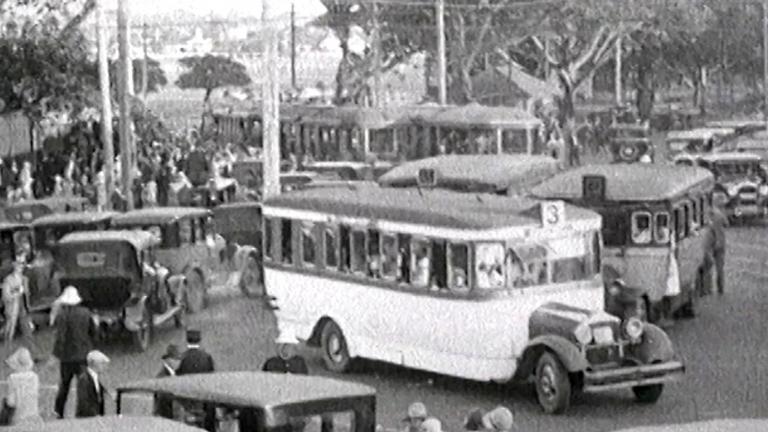 A picture from 1928 of ordered traffic chaos. Buses, trams and automobiles all crowd Anzac Parade Junction with fig trees in the background.