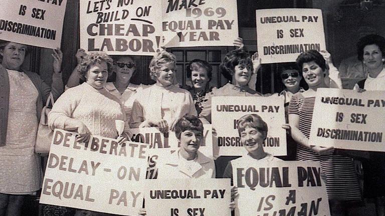 A demonstration in the 1970s featuring a group of women holding posters and placards demanding equal pay.