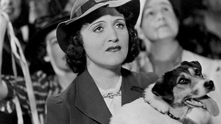 A crying Diana Du Cane holds a dog in her arms and looks upwards at a departing ship in a scene from The Broken Melody
