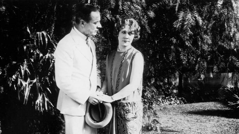 A man holds hands with Louise Lovely in a garden in a scene from the silent film Jewelled Nights.