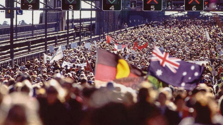 Huge crowd on the Sydney Harbour Bridge during the Walk for Reconciliation. Some people are waving Australian and Aboriginal flags. 