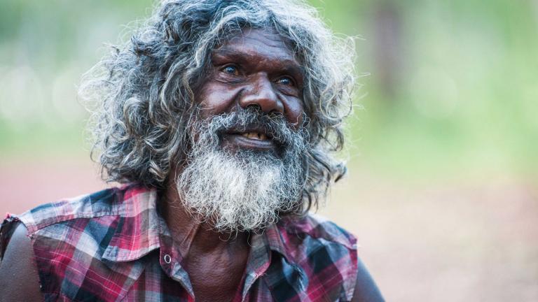 David Gulpilil in a production still from Charlie's Country. He is looking up and smiling. His hair and beard is going grey. 