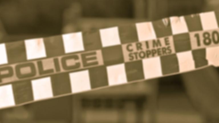 A sepia-toned shot of some checkered police tape with the words Police and Crime Stoppers written on it.