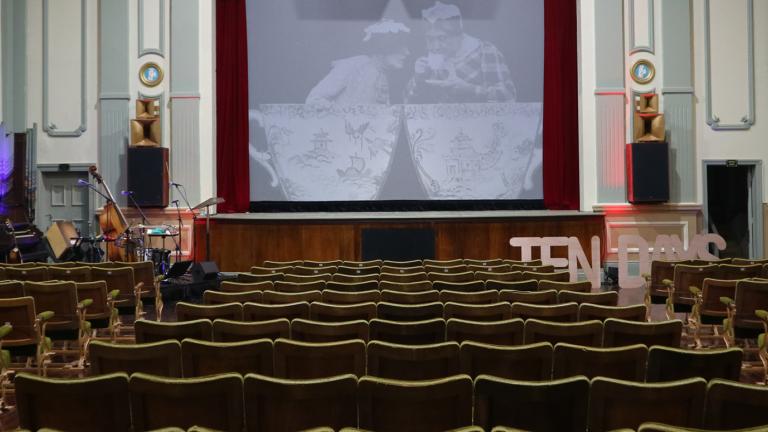 The interior of an old theatre. You can see the screen in the centre and rows of chairs facing it.