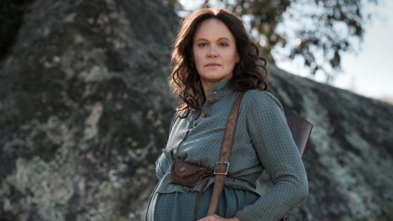 Leah Purcell as a pregrant bushwoman, standing outside in a rocky bush landscape in her film of The Drover's Wife