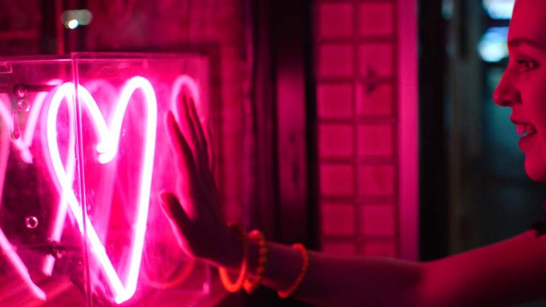 A woman holds out her hand to a neon-lit heart symbol
