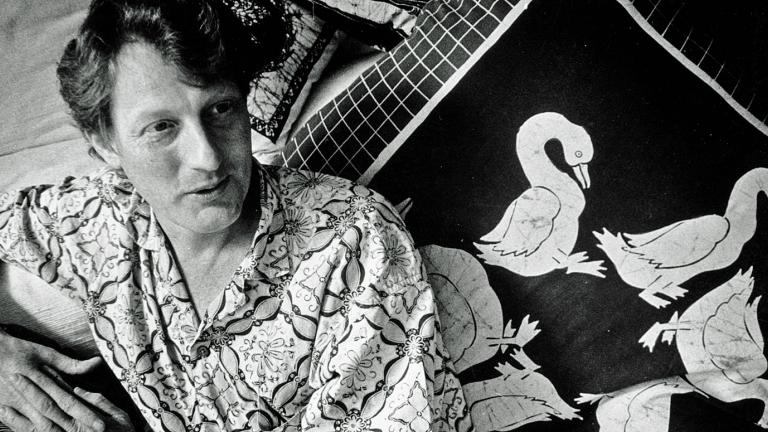 Australian documentary filmmaker, John Darling, pictured from waist up, wearing a Balinese shirt and leading against a cushion with images of birds on it.