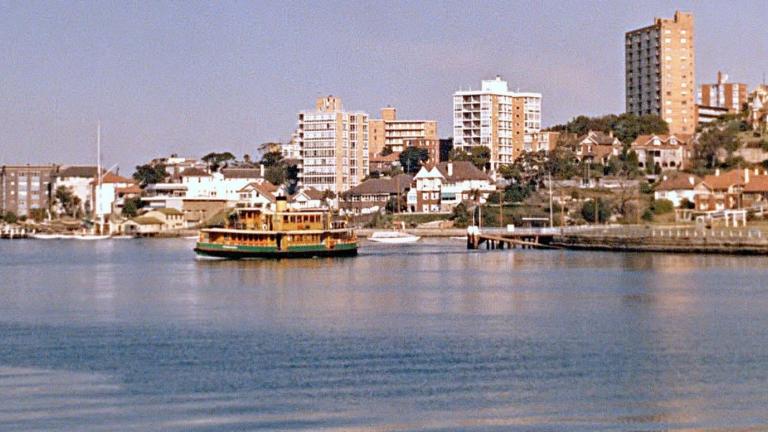A ferry is crossing Sydney Harbour with the shore and houses and apartments behind it.
