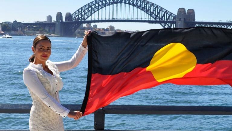 Cheree Toka holding an Australian Aboriginal flag. The Sydney Harbour Bridge is in the background.
