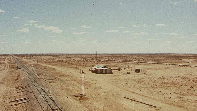An aerial shot of a hotel and railway line in a vast expanse of outback, in a scene from the 1971 film Wake in Fright