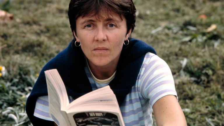 Helen Garner sitting in the ground, look at the camera and holding an open book