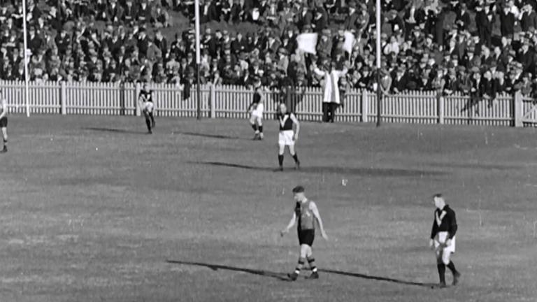 Black and white frame capture of the AFL goal umpire waving two flags signalling a six point score.