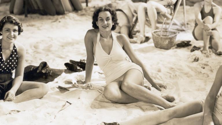 Women in swimsuits lounging on a film set made to look like a beach.