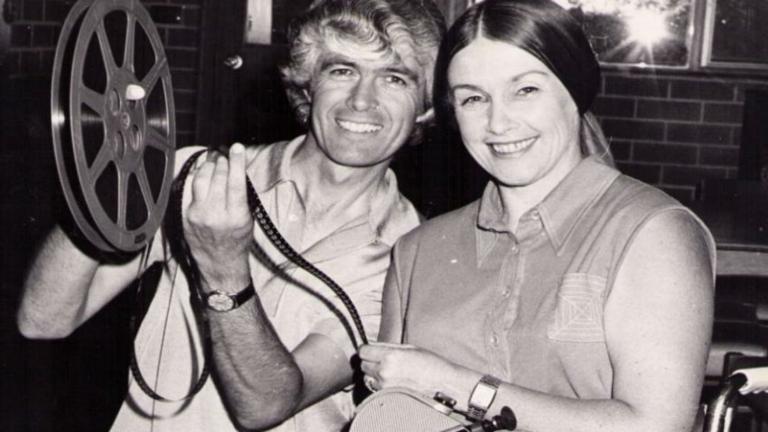 Don and Barbara Worley, 1975. Don holds film reel and Barbara is sitting in wheelchair holding movie camera.