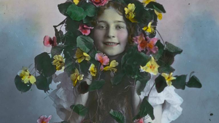 Glass slide image of a young girl peering through the centre of a wreath of flowers.