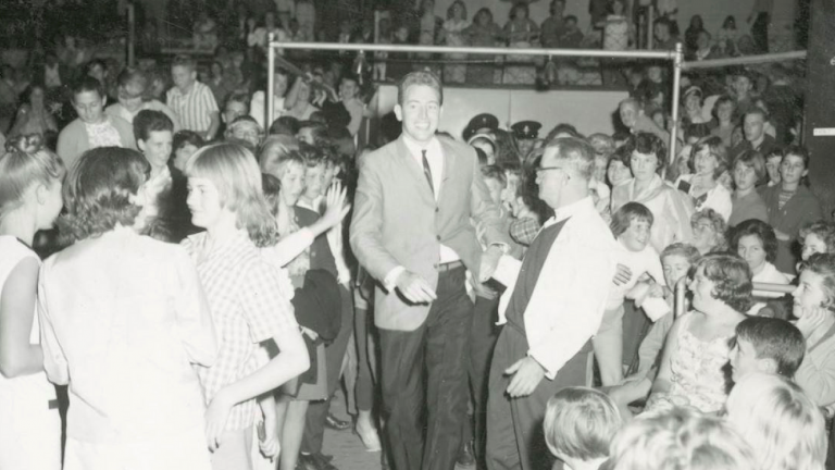 Popstar and TV personality Jimmy Hannan walking down the aisle at the Sydney Stadium with a crowd of people around him.