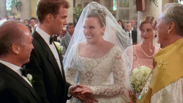 A scene from Muriel's Wedding where the main character, Muriel (Toni Collette) is getting married. She's standing at the alter with her groom, his best man, her bridesmaid and a minister.