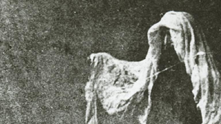 Black and white glass slide of a person with a sheet over their head pretending to be a ghost