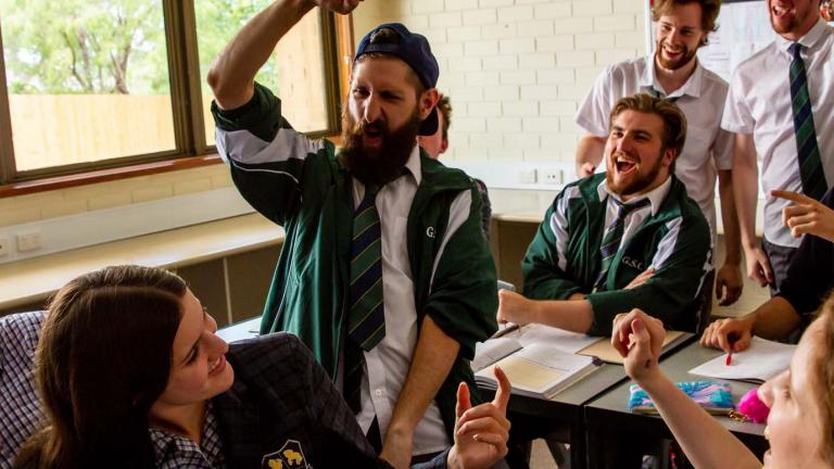 A group of high school students in uniform (including an older man with a beard) laughing and gesticulating 