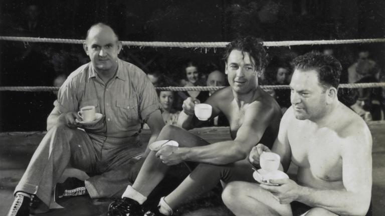 Referee Jim McMaster, Charles Farrell and professional wrestler Jack Clarke sitting in the middle of a wrestling ring drinking cups of tea Referee Jim McMaster, Charles Farrell and professional wrestler Jack Clarke sitting in the middle of a wrestling ring drinking cups of tea