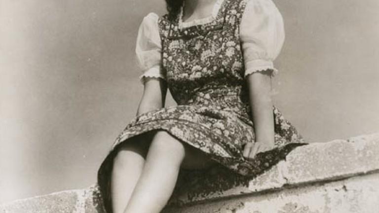 Merle Oberon sitting on a wall Publicity shot from below of Merle Oberon sitting on a wall, bare foot and wearing a floral dress.