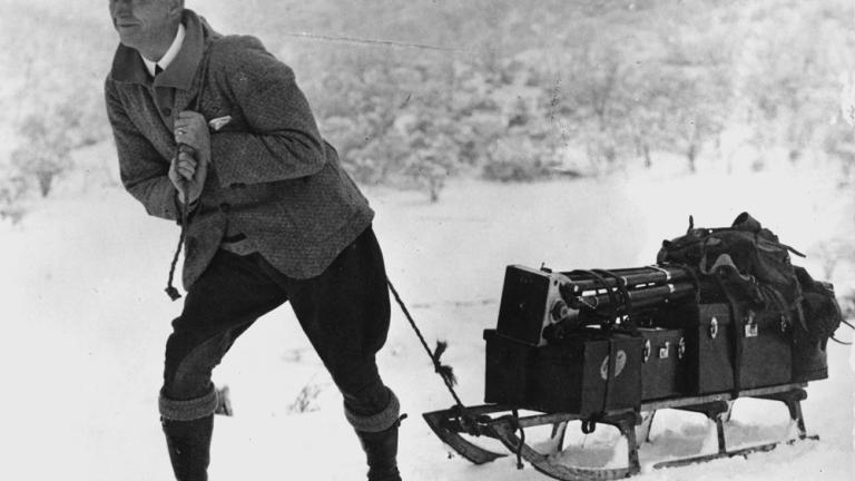 An unidentified member of the early Cinema and Photographic Branch pulls a sledge with equipment in the snow. An unidentified member of the early Cinema and Photographic Branch pulls a sledge with equipment in the snow.