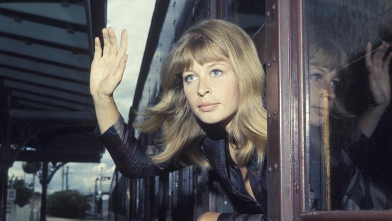 A young woman leans out the window of a train waving. A young woman leans out the window of a train waving.