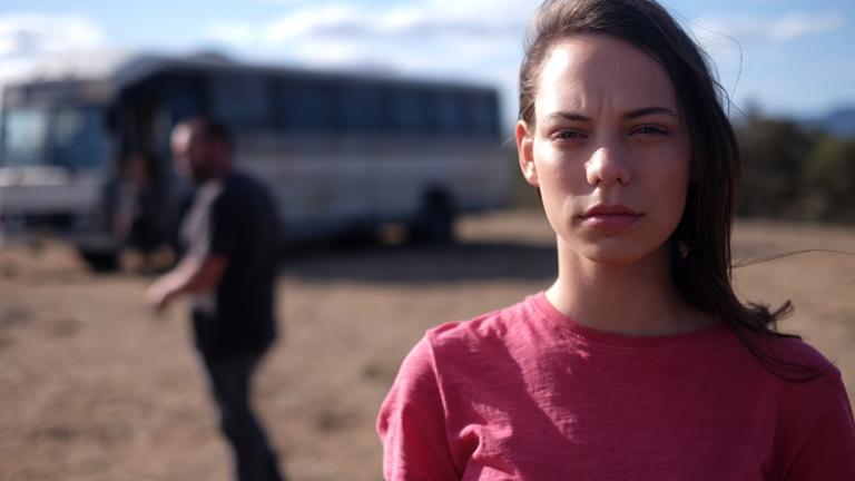 A woman close up to the camera with a man and bus in the background.