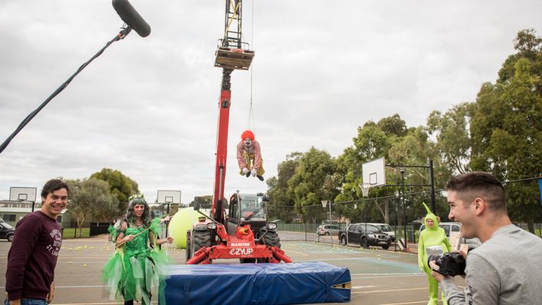 Crew on set. A clown is suspended from a crane.