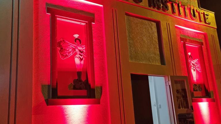 Exterior of an old theatre at night time with the front of the building lit up in red. 