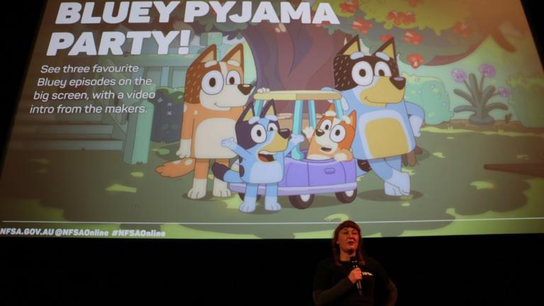 Welcoming kids to the Bluey Pyjama Party NFSA Public Programs Manager Karina Libbey in front of the Arc cinema screen, welcoming kids to the Bluey Pyjama Party. The screen shows a still image from the Bluey cartoon