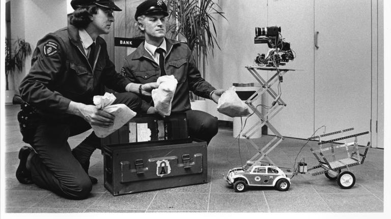 Armed guards held up by Malcolm's car - Lobby card