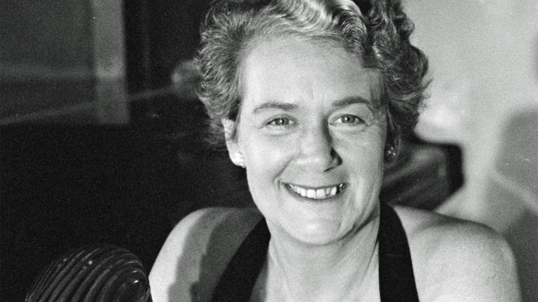 Head and shoulders shot of a woman smiling at camera with a radio mic in front of her.