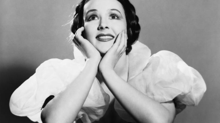 Actress Margot Rhys pictured from the waist up with her chin resting in her hands and looking upwards.