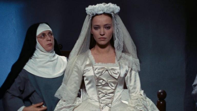 A young woman in a wedding gown stands centre of frame while a nun to her right looks at her intensely