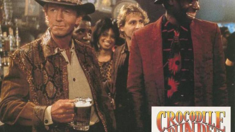 Crocodile Dundee German lobby card 11 Lobby card depicting Mick Dundee standing in a bar with a beer in his hand and a guy smiling next to him like Mick's just said something funny
