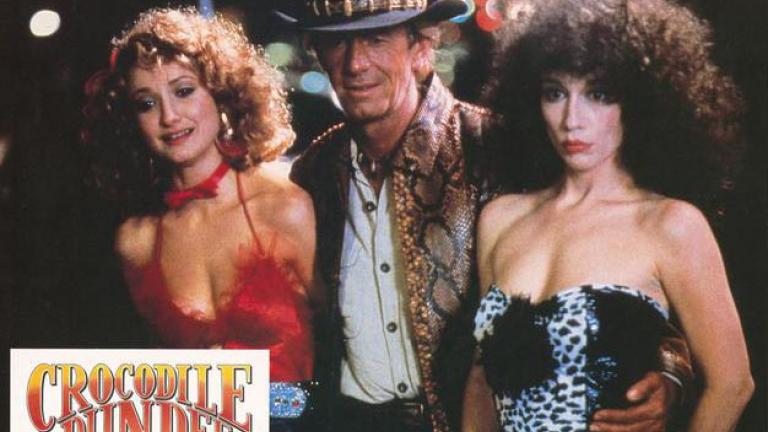 Crocodile Dundee German lobby card 12 Lobby card depicting Mick Dundee with his arms around two New York City prostitutes