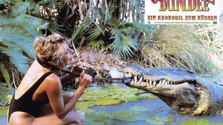 Crocodile Dundee German lobby card 4 German lobby card for Crocodile Dundee depicting Sue Charlton wrestling to get a water bottle off from around her neck because a crocodile has got a hold of it