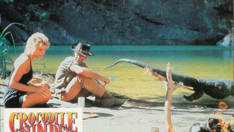Crocodile Dundee German lobby card 6 Lobby card depicting Linda Kozlowski as Sue Charlton and Paul Hogan's Mick 'Crocodile’ Dundee in the outback with a crocodile roasting on a spit made of tree branches