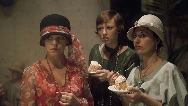 Film still of Lynette Curran as Maudie with her friends, played by Lorna Lesley and Vivienne Garrett wearing period costume and eating cake in the film, Caddie.
