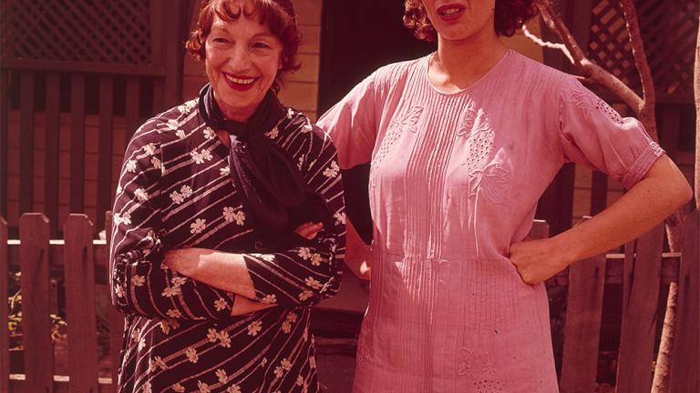 Film still with Helen Morse as Caddie standing with her hands on her hips next to an older woman wth arm folded outside a suburban house.