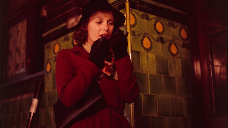 Film still of Helen Morse as Caddie applying lipstick as she walks along a street at night.