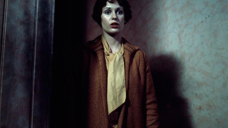 Film still of Helen Morse as Caddie walking into a dark room with a look of apprehension.