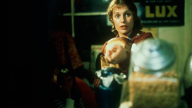 Film still of Helem Morse as Caddie seated in a shop holding one of her on screen children in her lap.