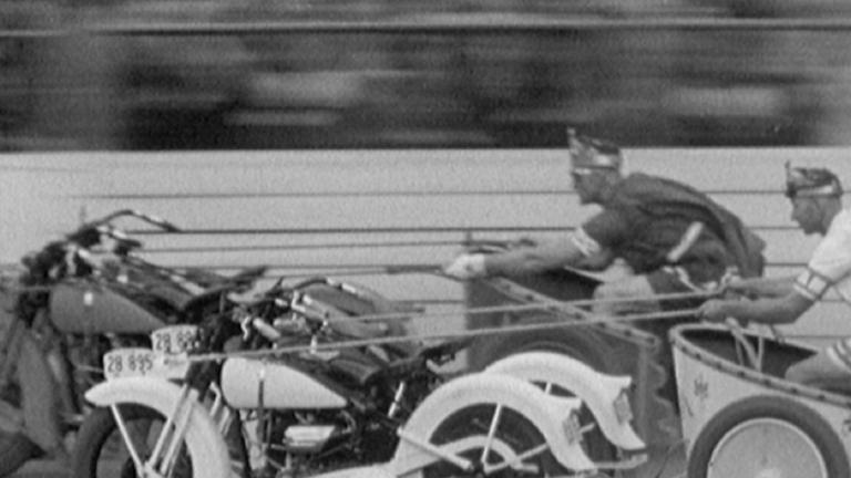 Two police officers in costume, riding their 'motorcycle chariots', Ben Hur style