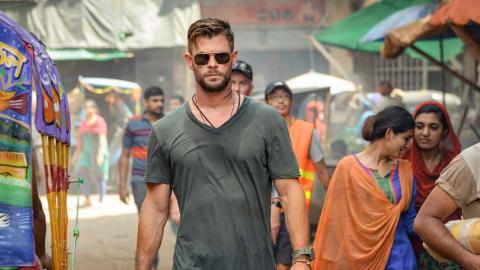 A caucasian assassin in t-shirt and sunglasses walks through a busy market in Bangladesh