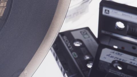 A reel to reel tape is in the foreground in front of three compact cassette tapes