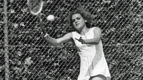 Evonne Goolagong-Cawley holding a wooden tennis racket and about to hit a tennis ball.