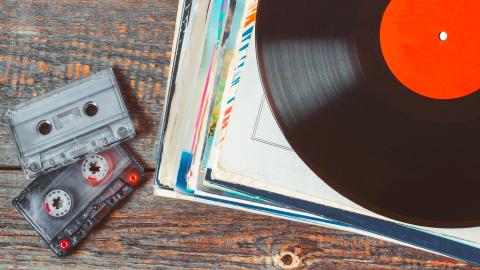 Audio cassette tapes and vinyl records stacked on a wooden table